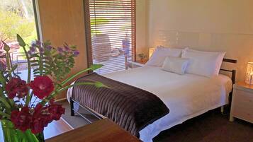 Une chambre à coucher comprenant un lit, des tables de chevet, une commode, une fenêtre avec des stores et un vase avec des fleurs.