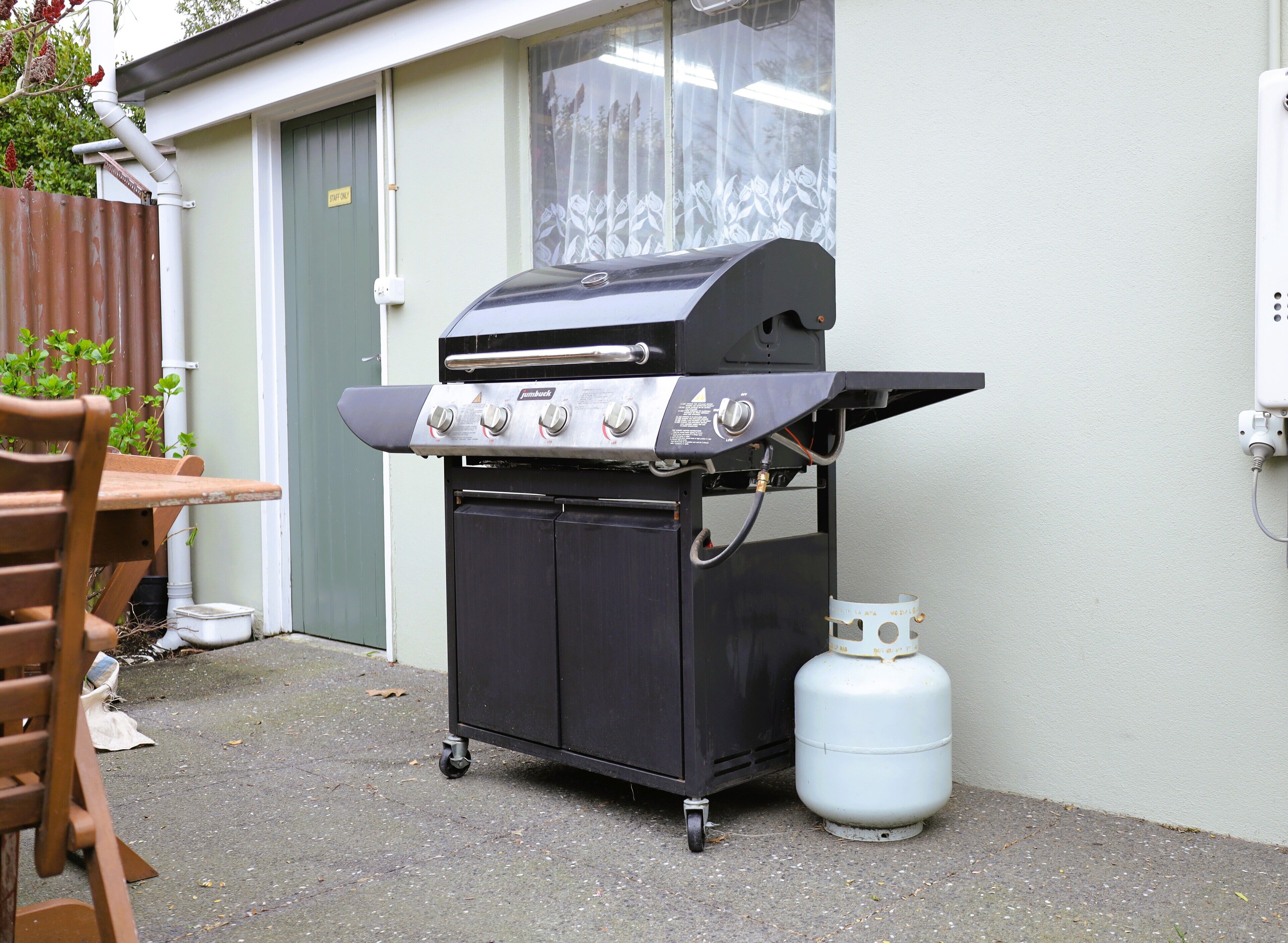 Una parrilla de gas portátil con cuatro quemadores, una repisa lateral y un tanque de gas.
