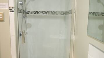 Una ducha con cerramiento de vidrio, cabezal de ducha de mano y llave empotrada en la pared.