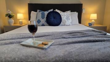 Cama bem arrumada com vários travesseiros, um copo de vinho tinto e um prato de biscoitos sobre a cama.