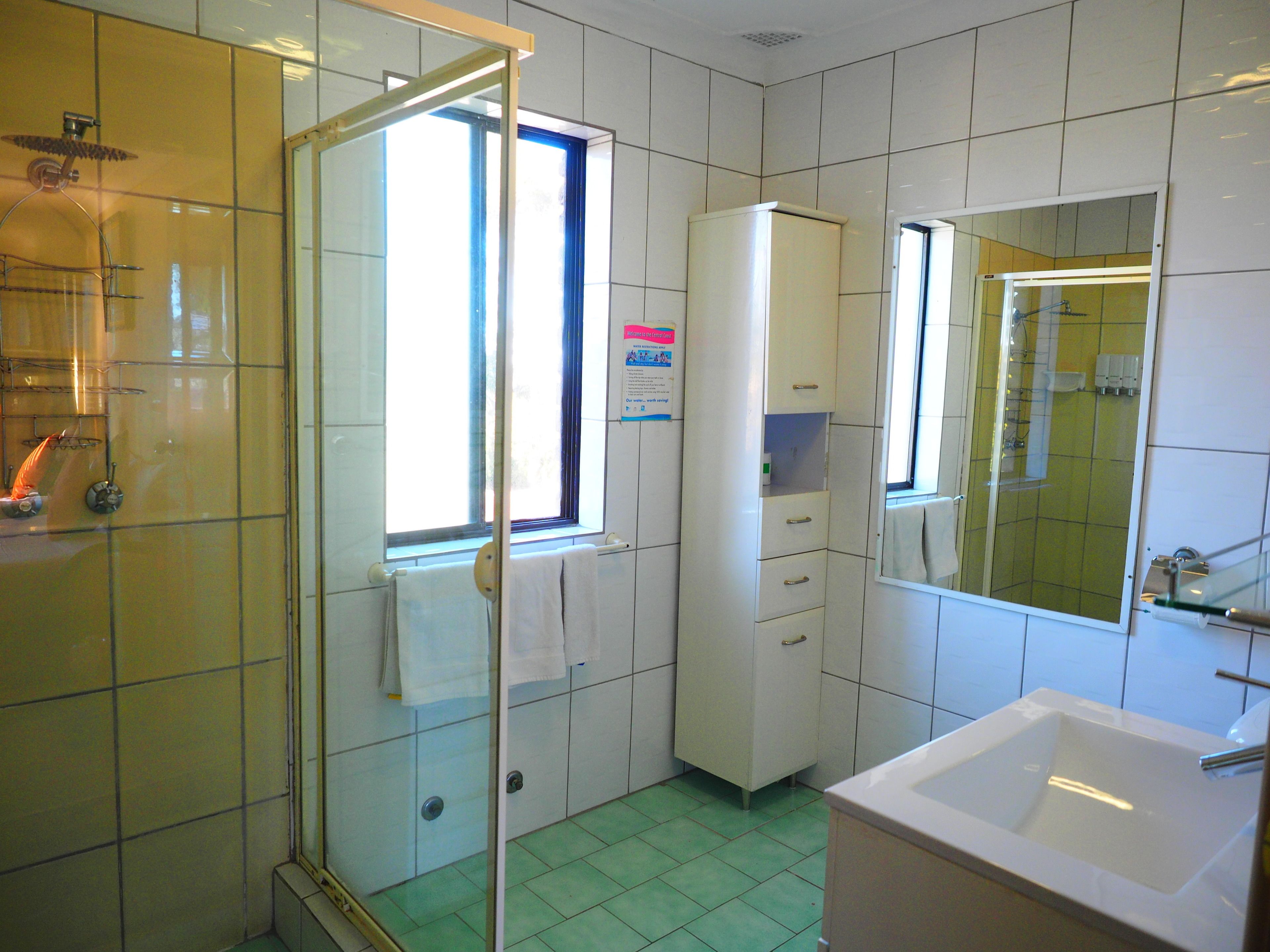 A bathroom with a glass shower enclosure, a white sink, and a cabinet with drawers.