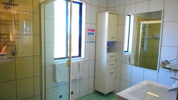 A bathroom with a glass shower enclosure, a white sink, and a cabinet with drawers.