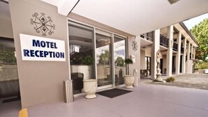 Een moderne hotel receptie met een glazen ingang, een naambord en een standbeeld.