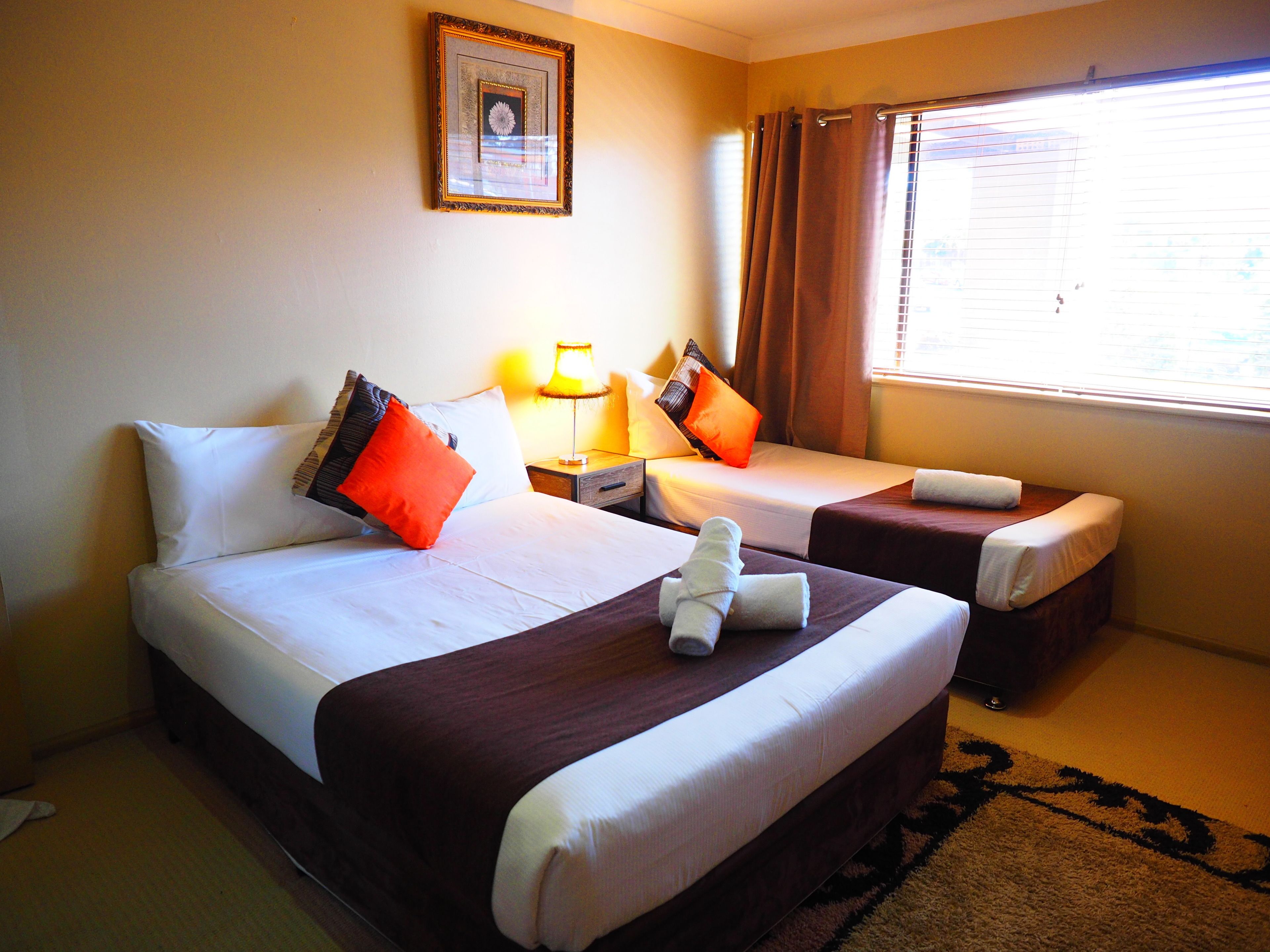 A hotel room with two beds, a framed picture on the wall, a window with curtains, and a lamp on the nightstand.
