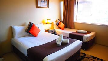 A hotel room with two beds, a framed picture on the wall, a window with curtains, and a lamp on the nightstand.