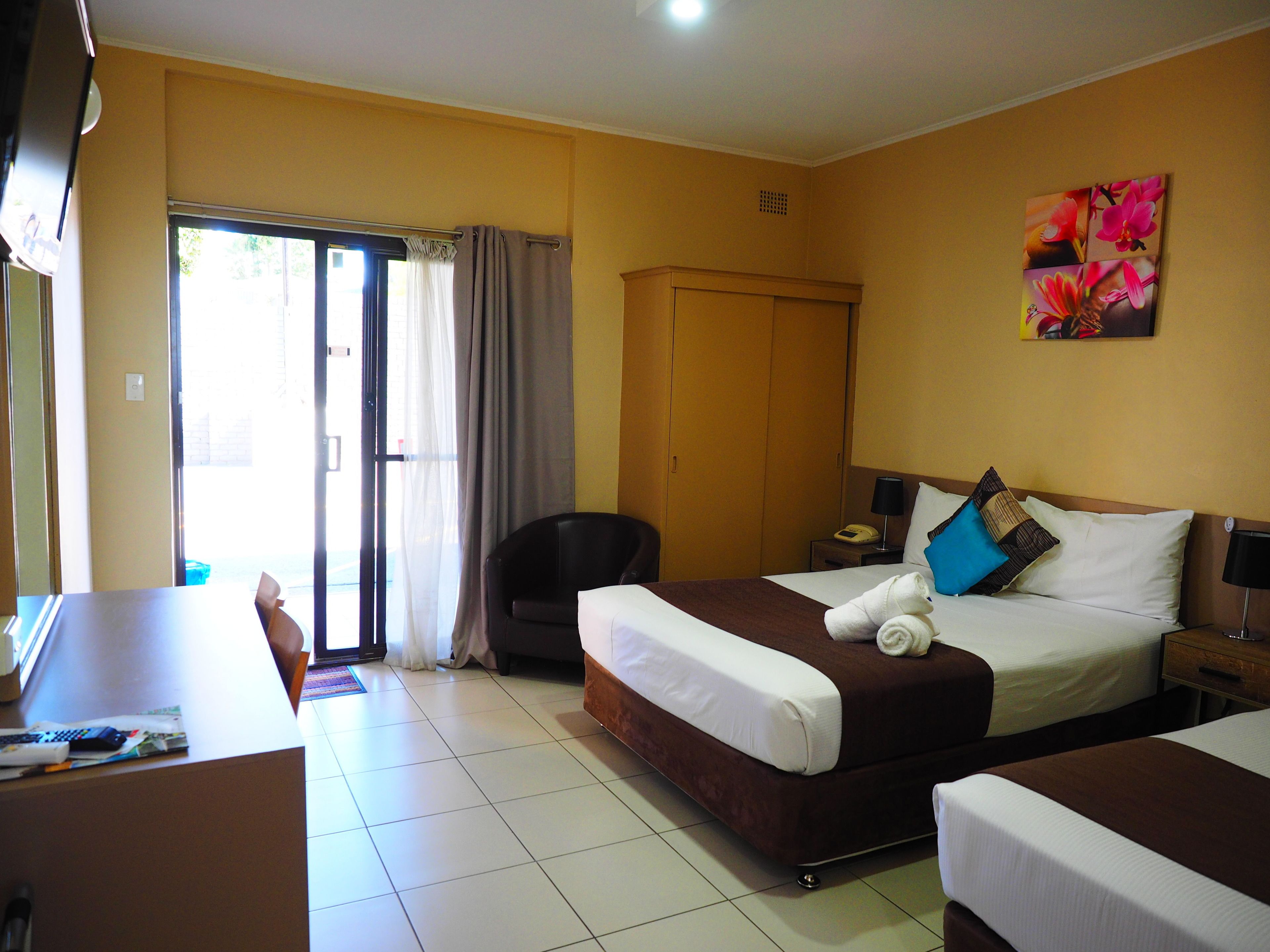 A hotel room with a bed, a desk, a chair, a wardrobe, and a painting on the wall.