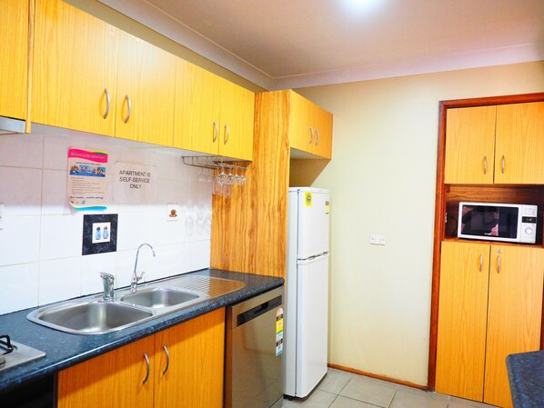 A compact kitchen with wooden cabinets, a stainless steel sink, a white refrigerator, and a built-in microwave.