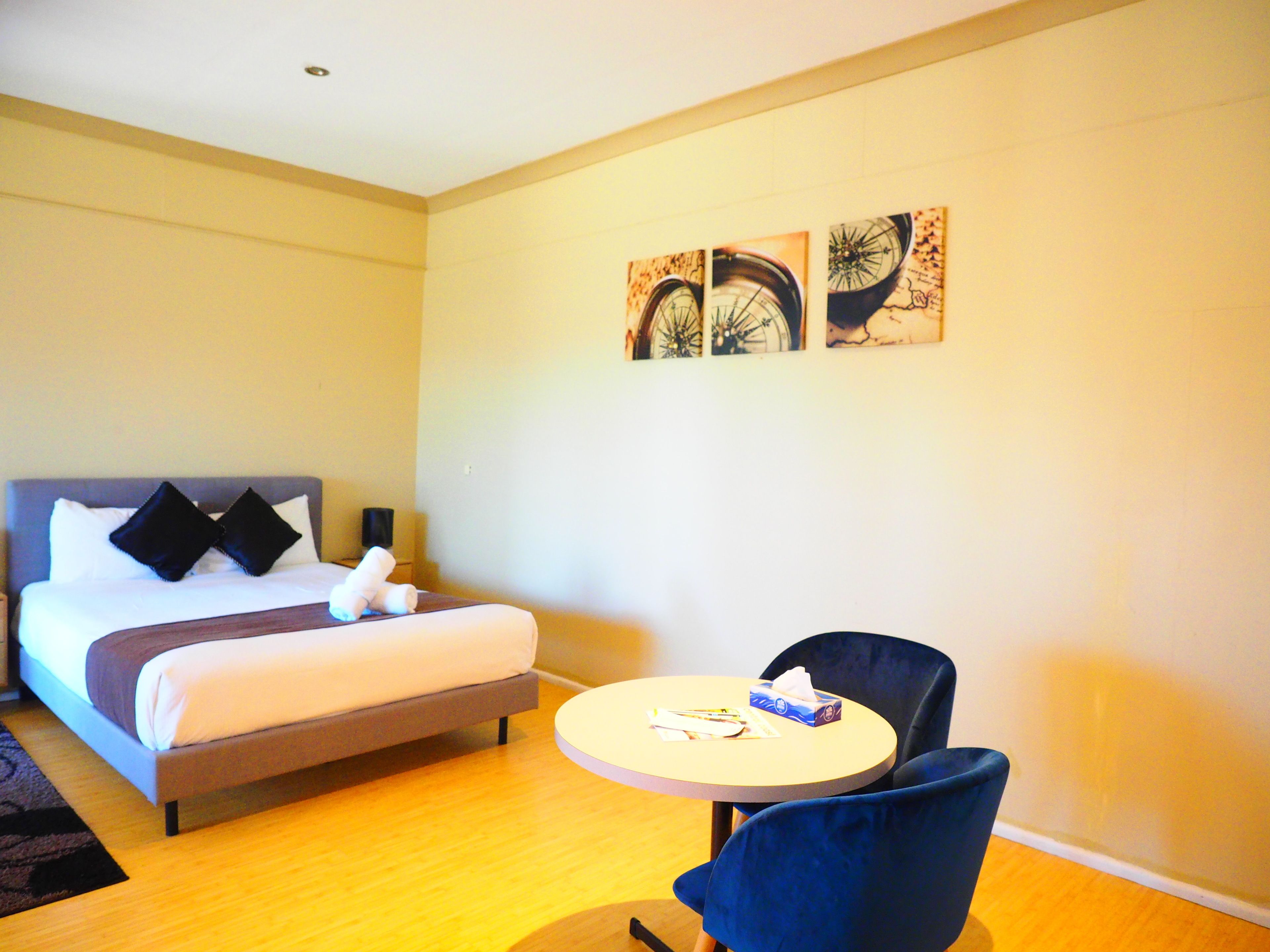 A hotel room with a bed, a round table with a chair, and three wall-mounted artworks.