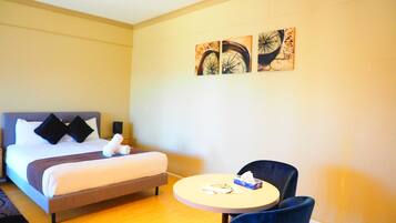 A hotel room with a bed, a round table with a chair, and three wall-mounted artworks.