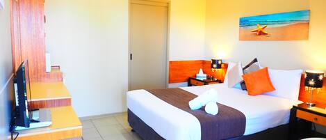 A hotel room with a bed, a desk, a chair, a TV, a painting of a beach, and a staircase.