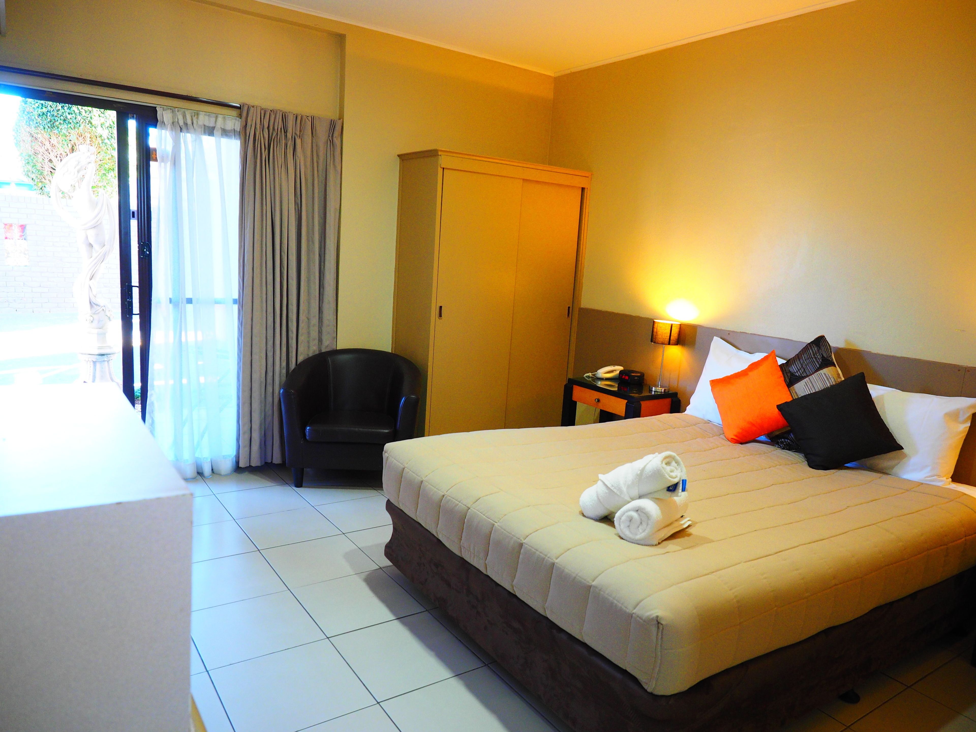 A hotel room with a bed, a chair, a desk, a lamp, and a wardrobe.