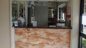 Uma área de recepção com balcão de mármore, uma porta com aviso de 'Proibido Fumar' e vista do interior através de uma porta de vidro.