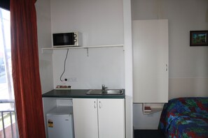 A compact room with a kitchenette, including a microwave, sink, and small refrigerator. There is a bed with a colorful blanket and a framed picture on the wall. - Linwood Lodge Motel (Greenwich)