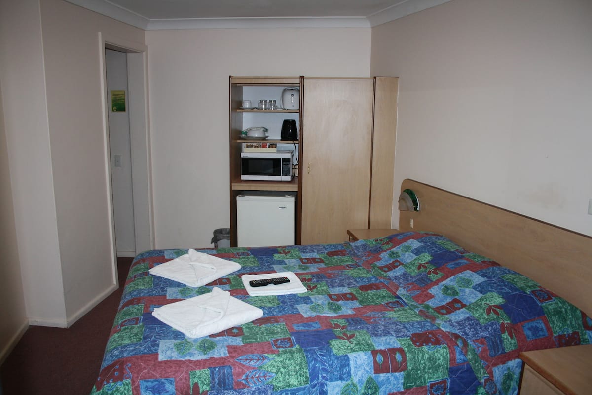 A hotel room with a bed, a microwave, a refrigerator, and a wooden wardrobe.