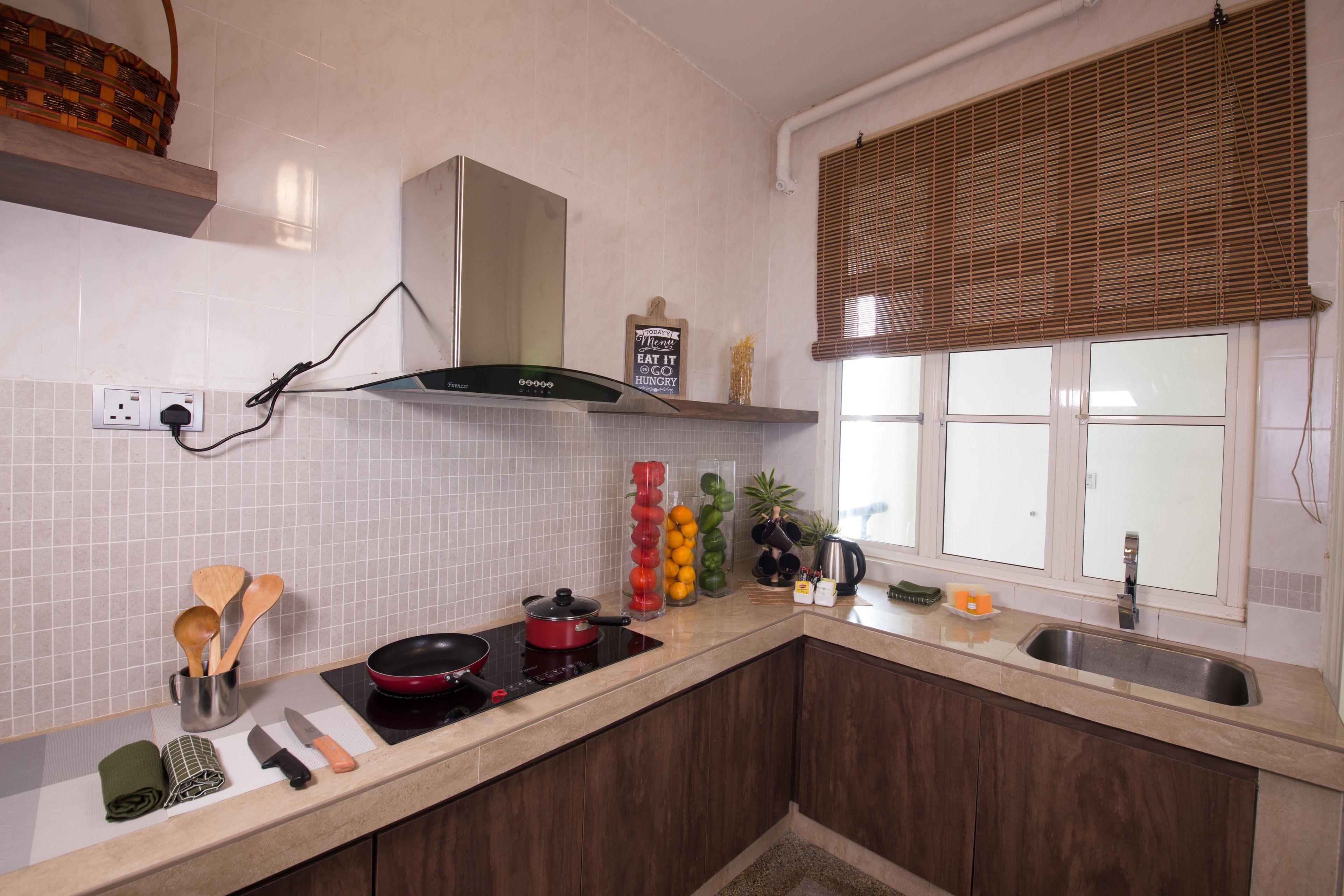 A kitchen with white tiled walls, a stainless steel range hood, a built-in oven, a sink, and a window with blinds.