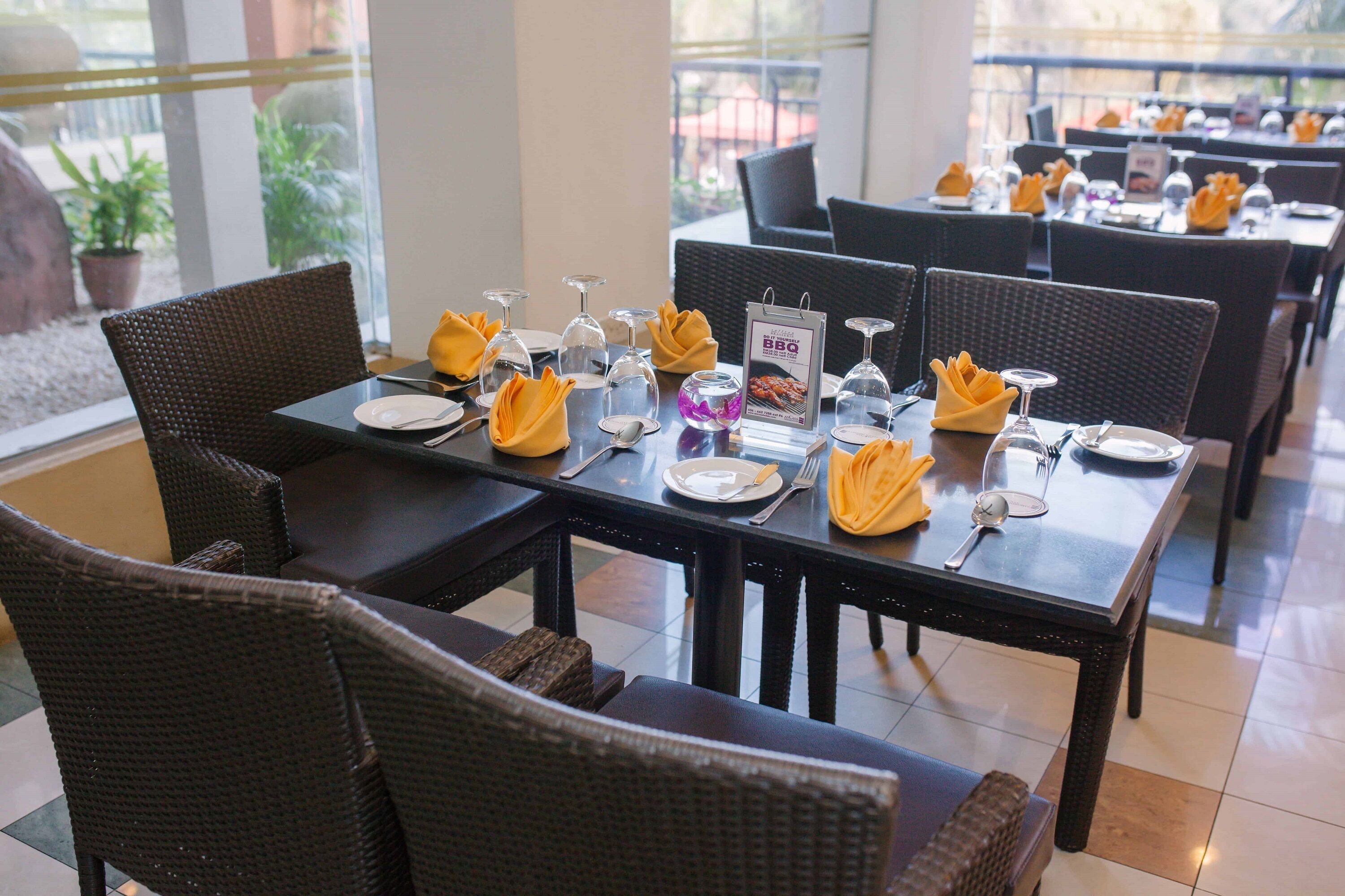 A dining area with tables set for service, featuring wicker chairs and yellow napkins.