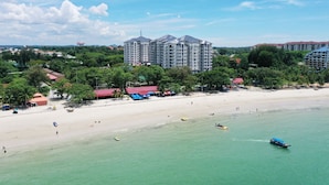 Ein Strandhotel mit mehreren Gebäuden, einem Sandstrand und klarem türkisblauem Wasser.