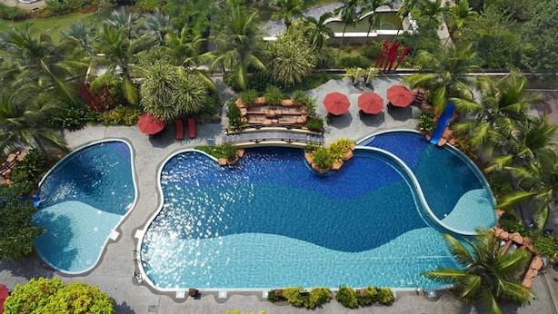 Eine Vogelperspektive eines Resorts mit einem großen, zentralen Pool, umgeben von Palmen und Grünpflanzen.