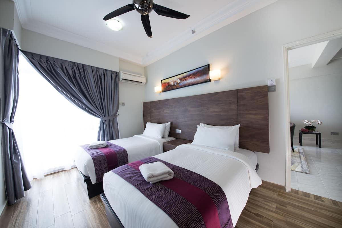 A hotel room with two beds, a ceiling fan, an air conditioning unit, a painting on the wall, and a view of the outside.
