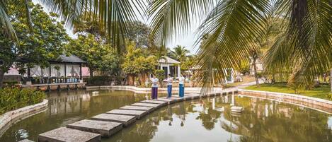 A tranquil garden with a pond, stone stepping stones, and palm trees.