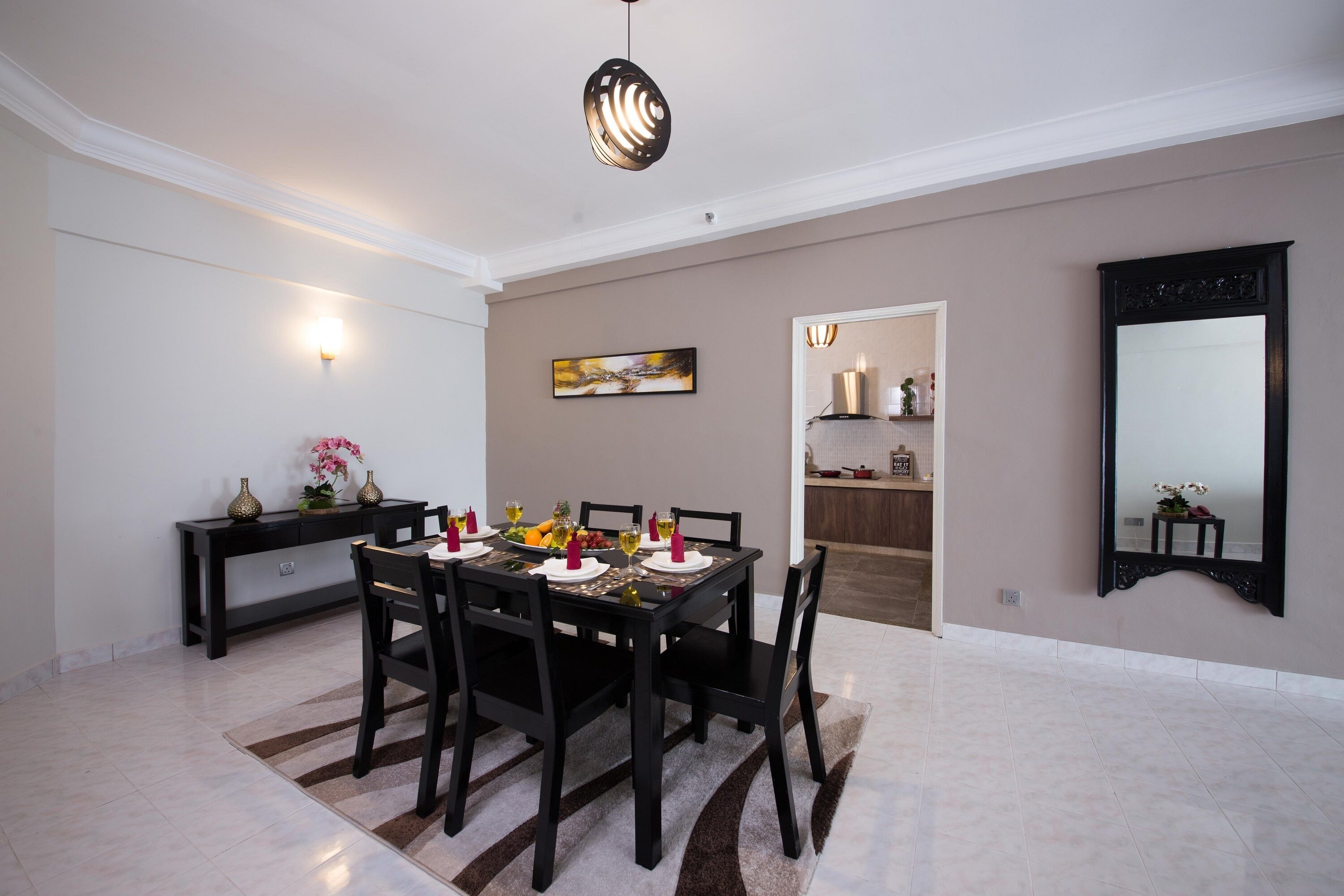A dining area with a table set for six, a dark wooden console table with decorative items, a painting on the wall, and a large mirror.