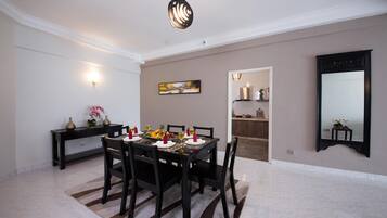 A dining area with a table set for six, a dark wooden console table with decorative items, a painting on the wall, and a large mirror.