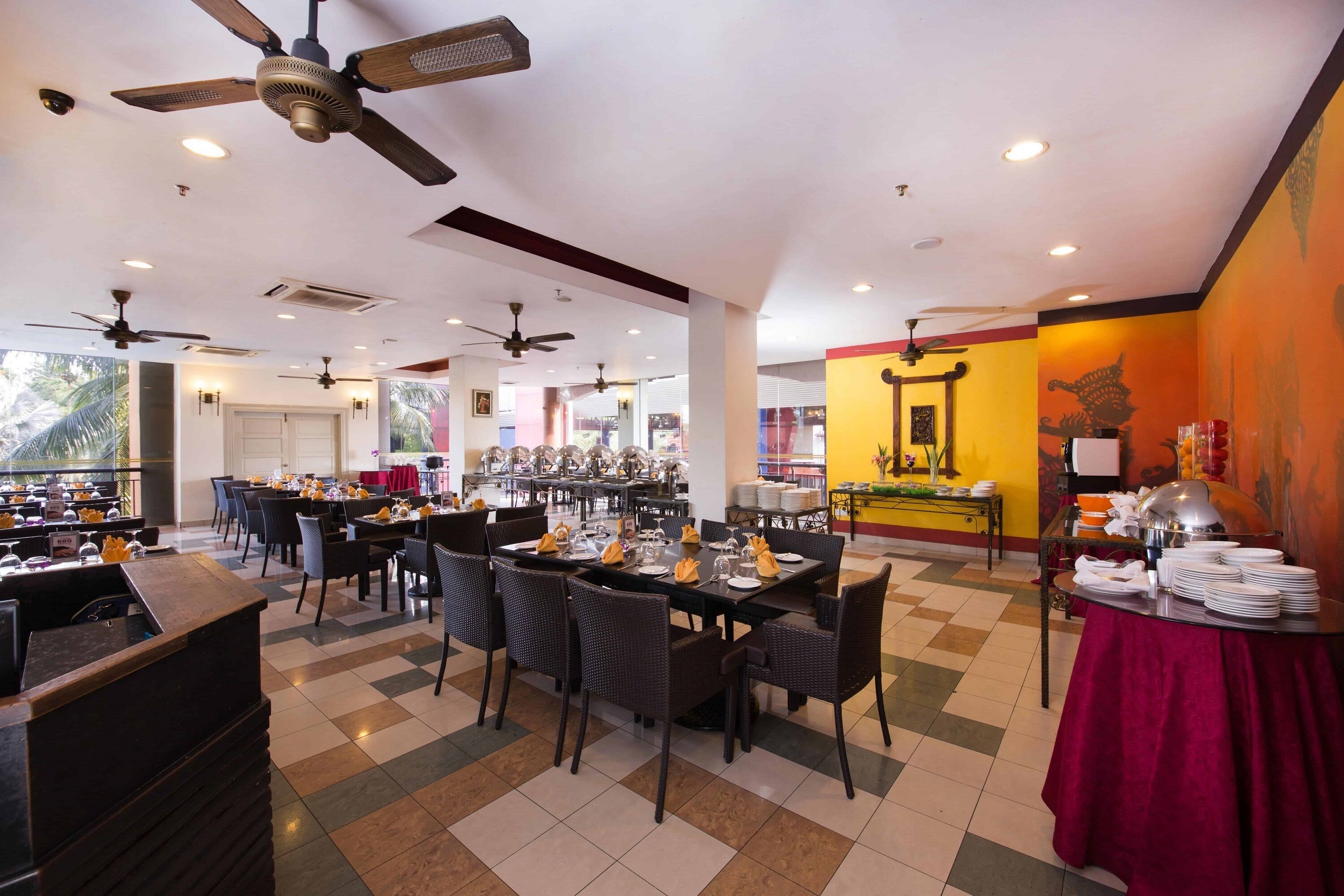 Un comedor amplio con varias mesas y sillas, ventiladores de techo y un sistema de buffet.