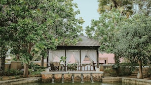 Ein friedlicher Garten mit einem kleinen Pavillon, einem Wasserspiel aus Stein und üppigem Grün.