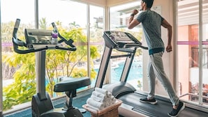 Ein Fitnessraum mit Laufband und Crosstrainer, einer Wasserflasche und einem Wäschekorb mit Handtüchern.