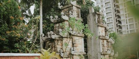 Una estructura de piedra con intrincados grabados, rodeada de vegetación exuberante y un muro de ladrillo.