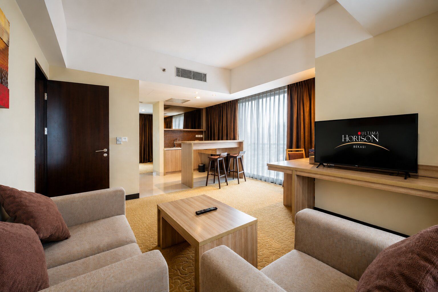 Una habitación de hotel con sala de estar, kitchenette, televisor y puerta.