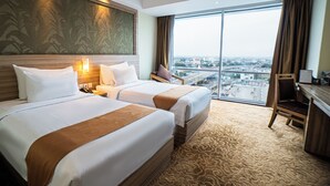 A hotel room with two beds, a desk, and a large window offering a city view. - Horison Ultima Bekasi (Bekasi)