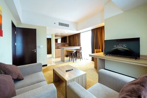 A modern hotel room with a living area, a dining area, and a TV on the wall.