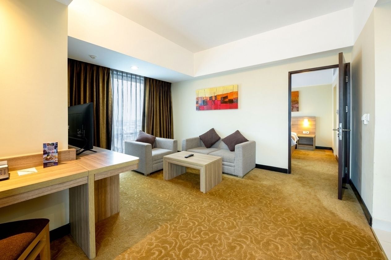 A hotel room with a desk, two armchairs, a coffee table, a TV, and a painting on the wall.