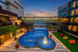 An outdoor swimming pool with a fountain, surrounded by a green lawn and potted plants. - Horison Ultima Bekasi (Bekasi)