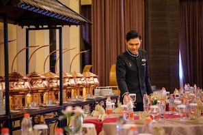 A hotel dining area with a buffet setup, including copper serving pots and a table with water bottles and napkins. - Horison Ultima Bekasi (Bekasi)