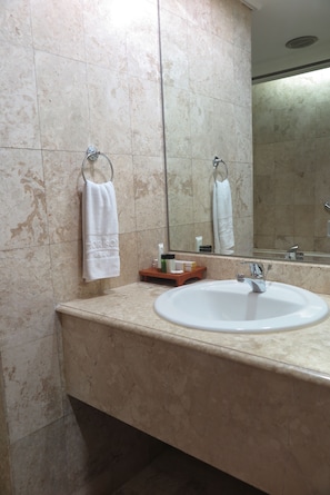 Une salle de bain avec un lavabo en marbre, une serviette suspendue à un porte-serviettes en forme d’anneau et un miroir qui reflète la salle de bain.