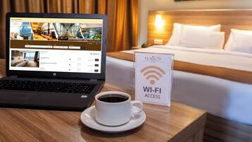 Una computadora portátil mostrando una página de reservas de hotel, una taza de café y un cartel que indica acceso a Wi-Fi.
