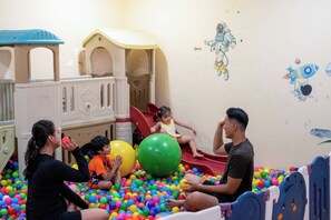 Un área de juegos con un tobogán, una piscina de pelotas y una pared decorada con motivos espaciales.