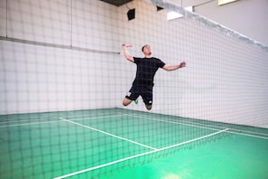 Un court de tennis avec un filet, un joueur en plein mouvement et un mur orné d’un motif quadrillé.