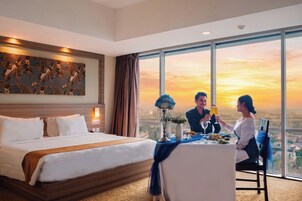 A hotel room with a large bed, a dining table with a view, and a painting on the wall.