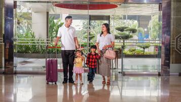 A family with a child in a hotel lobby with a glass door entrance, a red ceiling, and indoor plants.