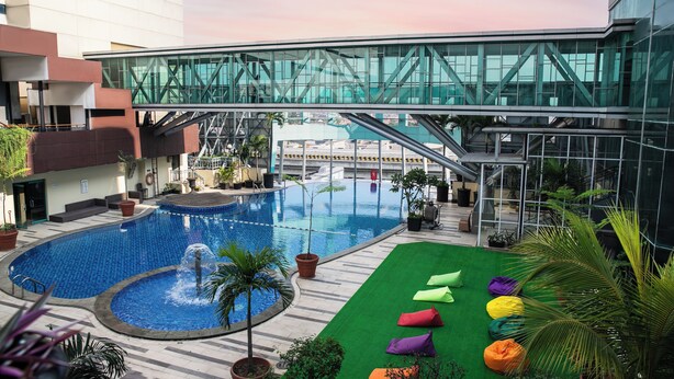 A rooftop pool with a glass bridge, surrounded by potted plants and colorful bean bags. - Horison Ultima Bekasi (Bekasi)
