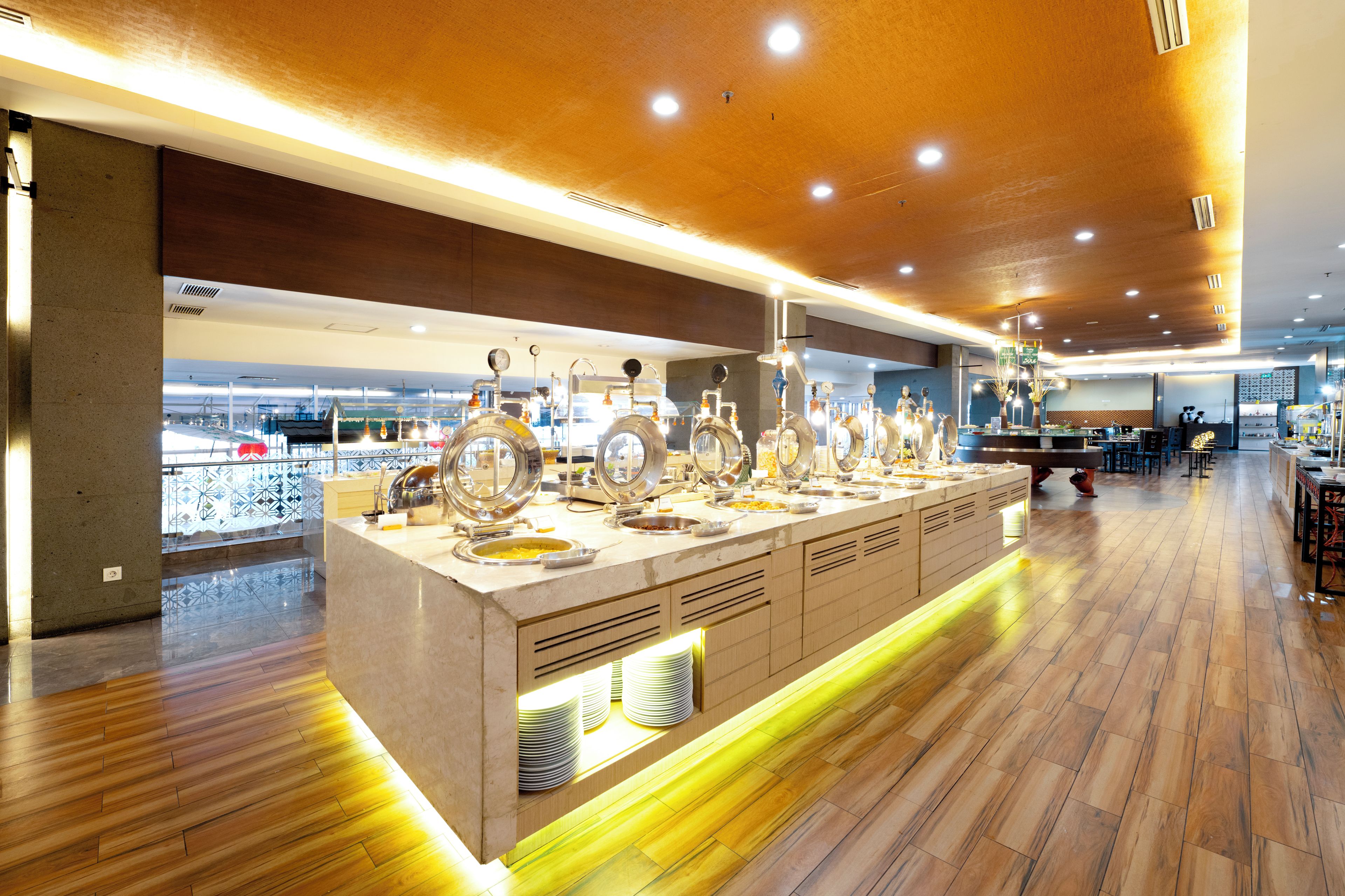 A buffet area with a variety of food options, a counter with plates, and a view of the cityscape through large windows.