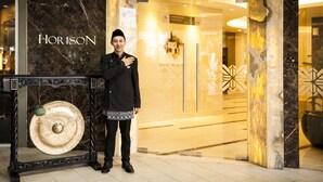 A man standing in front of a hotel entrance with a marble facade and a sign that reads "HORIZON". - Horison Ultima Bekasi (Bekasi)