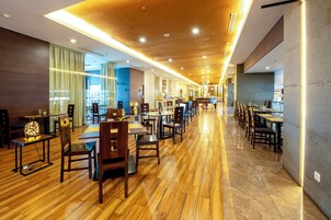 A modern hotel lobby with wooden flooring, multiple dining areas, and a long corridor with tables and chairs.