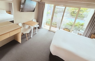 A hotel room with a bed, a desk, a chair, a TV, and a sliding glass door leading to a pool area.