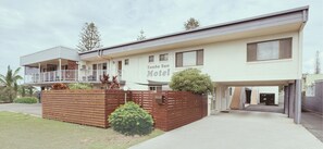 A two-story motel with a balcony on the upper floor, a covered parking area, and a small garden with a wooden fence and a Christmas tree. - Yamba Sun Motel (Yamba)
