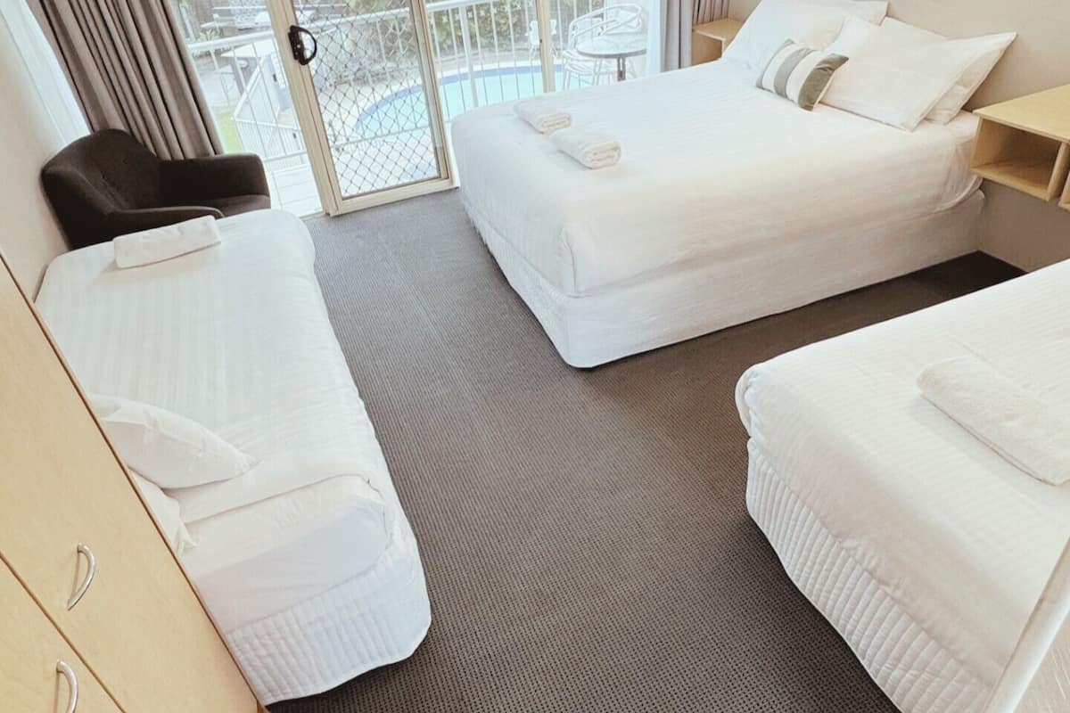 Ein Hotelzimmer mit zwei Einzelbetten, einem kleinen Tisch, einem Stuhl und einer Glastür, die zu einem Außenbereich führt.