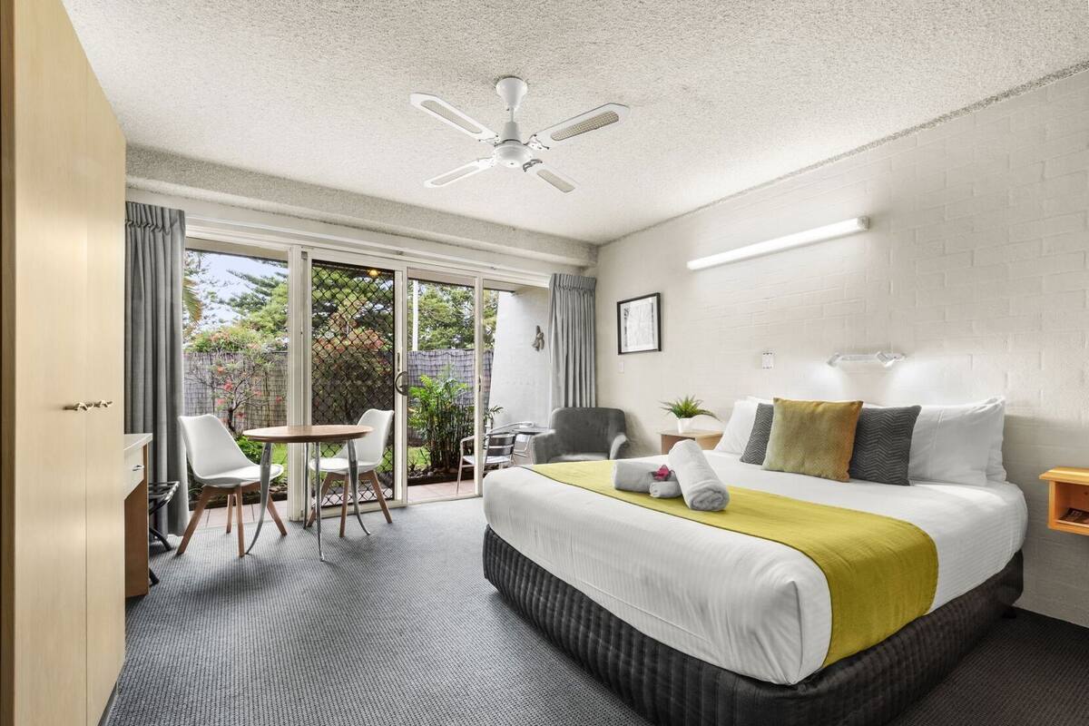 Ein Hotelzimmer mit Bett, Schreibtisch, Stuhl, Deckenventilator und Blick ins Freie.